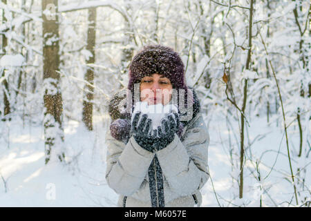 Hält eine Frau eine Handvoll Schnee in den Händen und bläst. Winter im Wald. Die sonne funkelt. Tag, Russland. Stockfoto