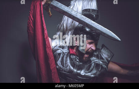 Roman Gladiator, Wrestler und Krieger von Rom mit Helm und roten Mantel, trägt ein Schwert, Bart und lange Haare. Stockfoto