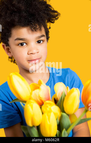 Adorable kleinen Jungen mit einem blauen T-Shirt mit einem Tulpen Bouquet. Auf gelb isoliert Stockfoto