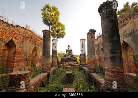 Alte Tempel Ruinen und alte Statue eines sitzenden Buddha gesehen von der Vorderseite der Yadana Hsemee Pagode Komplex in Inwa (Ava) in der Nähe von Mandalay in Myanmar. Stockfoto