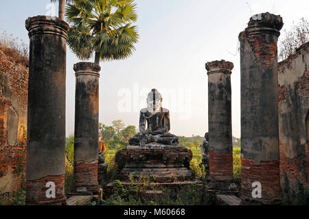 Alte Tempel Ruinen und alte Statue eines sitzenden Buddha gesehen von der Vorderseite der Yadana Hsemee Pagode Komplex in Inwa (Ava) in der Nähe von Mandalay in Myanmar. Stockfoto