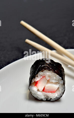 Sushi auf einem weißen Teller: Maki (Rolle in Algen umwickelt) und Stäbchen Stockfoto
