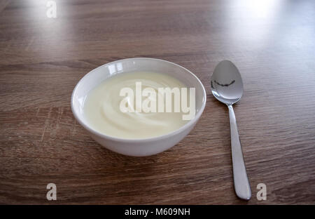 Keramische Schüssel aus weißem Joghurt auf hölzernen Hintergrund und Löffel mit Joghurt Blick von oben, Joghurt isoliert. Joghurt Joghurt Stockfoto