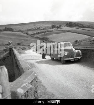 1950, historische, Irland, sanfte Hügel, auf einer ruhigen Landstraße einen Treiber vor seinem Auto an einer Brücke an der Blick aussieht. Stockfoto