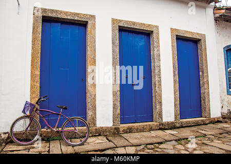 Paraty, Brasilien. Fahrrad vor blauen Türen und Stein Bürgersteig in Paraty, einer historischen Stadt im Staat Rio de Janeiro Küste erhalten. Stockfoto