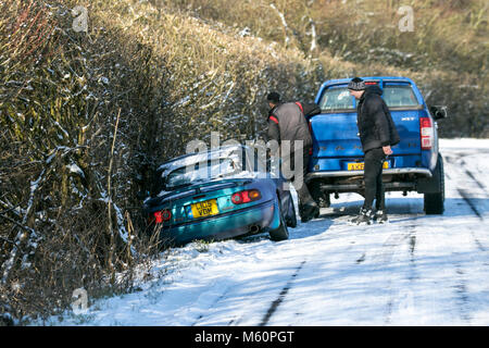 Burscough, Merseyside, Großbritannien. Februar 2018. Wetter in Großbritannien. Rutschen auf Eis, Winterwagenunfall, Straße, Schnee, Kälte, Gefahr, Eis, Verkehr, Fahrzeug, Wetter, Transport, Straße, Sicherheit, Reisen, da das Biest aus dem Osten schwierige und tückische Fahrbedingungen verursacht. Ein Lastwagen hält an der Seite eines abgestürzten Autos, das in der Nähe von Burscough, Merseyside, Großbritannien, auf der Straße abrutscht. Stockfoto