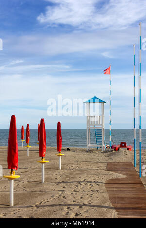 Leere Sandstrand mit geschlossenen roten Sonnenschirmen, eine Promenade und ein Rettungsschwimmer Wachtturm Stockfoto