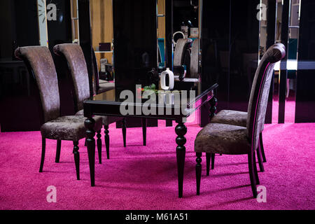Shop, Verkauf von Möbeln auf den Vertriebsbereich. Esstisch ist schwarz glänzend Farbe mit barchannyh vier Stühle auf einem Spiegel Hintergrund und rosa Teppich. Stockfoto