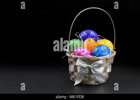 Bunte Ostereier im Korb auf schwarzen Hintergrund isoliert. Stockfoto