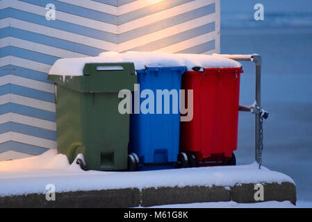 Mehrfarbige Müll- und Recyclingbehälter, die in Schnee am Southend an der Meeresküste bedeckt sind. Mehrfarbig Stockfoto