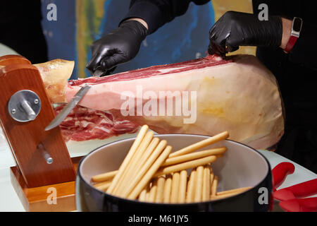 In Scheiben geschnittene Getrocknete chamon Prosciutto. Ein Mann schneidet einen jamon, ein in warmen Farbtönen. Selektiver Fokus. Stockfoto