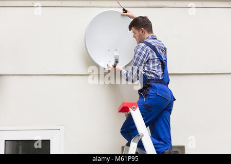 Junge männliche Techniker in Uniform Installation TV Satellitenschüssel auf Wand Stockfoto