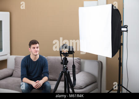 Junge männliche Blogger Sitzen auf einem Sofa Aufzeichnen von Videos mit der Kamera zu Hause. Stockfoto