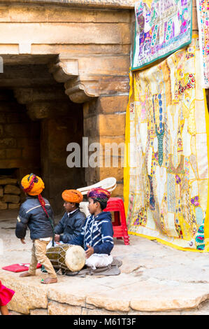 Jaisalmer, Indien - 28 Dez 2018: Kinder in typische Rajasthani indianische Kleidung spielen mit einer Trommel in der Mitte einer Festung mit Steinmauern Stockfoto