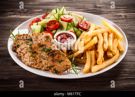 Gebratenes Schweinekotelett, gekochte Kartoffeln und Gemüse Salat auf hölzernen Tisch Stockfoto