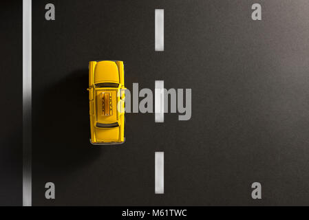 Yellow cab Spielzeugauto auf einem schwarzen Hintergrund wie Asphalt. Stockfoto