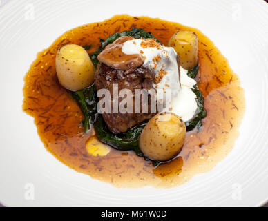Rossini-Rinderfilet mit jungem Spinat und eingelegtem Foie Gras ist der Hauptgang des Kartoffelmenüs, das der deutsche Michelin-Sterne-Koch Sebastian Prüßmann im Hotel und Restaurant Kronenschlösschen in Hattenheim, Eltville am Rhein, Hessen, Deutschland, zubereitet. Das Filet liegt auf Spinat in einem bernsteinfarbenen Jus. Eine Scheibe Foie Gras, eine weiße Sauce und goldene Krümel krönen es. Drei kleine gekochte Kartoffeln stehen um das Fleisch herum. Das klassische Gericht ist nach dem Komponisten Gioachino Rossini benannt. Es wird begleitet von den Rotweinen 2013 Allesverloren Tinta Barocca und 2014 Allesverloren Shiraz aus der Swartland. Im Sou Stockfoto