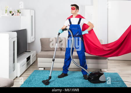 Superhelden Hausmeister Reinigung Teppich mit Staubsauger im Wohnzimmer Stockfoto