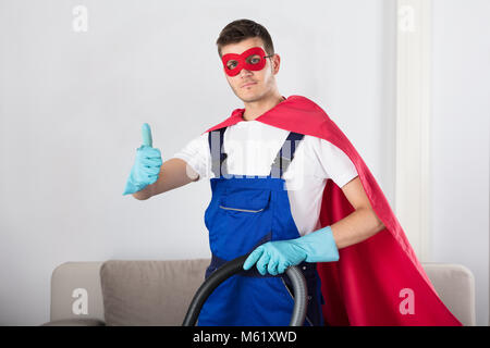 Superhelden Hausmeister mit Staubsauger, Daumen hoch, im Wohnzimmer Stockfoto