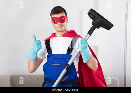 Superhelden Hausmeister mit Staubsauger, Daumen hoch, im Wohnzimmer Stockfoto