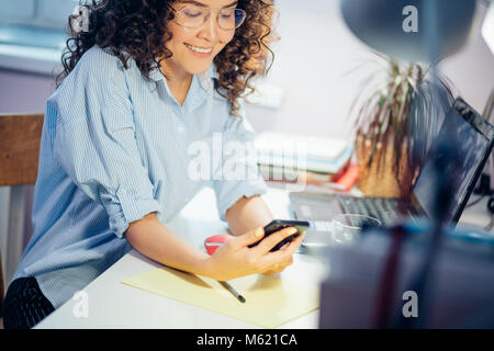 7/8 Foto der jungen Frau, die in einer zwanglosen Textilien holding Schwarz Handy im Innenbereich Stockfoto
