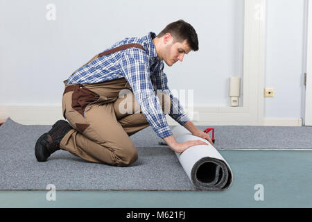 Junge männliche Heimwerker Rolling Teppich auf dem Boden zu Hause Stockfoto