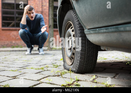 Sorgen junger Mann mit der Hand auf den Kopf und zeigte auf eine Reifenpanne Reifen Geduckt Stockfoto