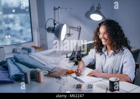 Lachende Frau Notizen am Tisch Tailor's am Abend Stockfoto