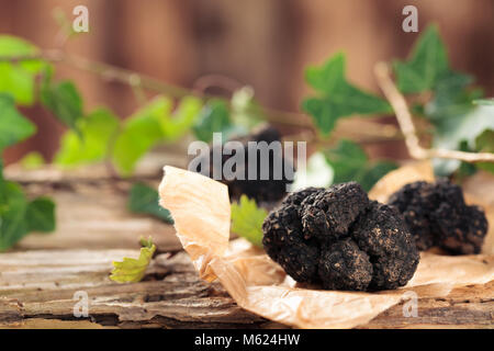 Schwarze Trüffeln und Blätter auf alten Holztisch. Stockfoto