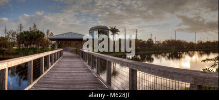 Sonnenuntergang über Pavillon auf einer hölzernen abgeschiedenen, ruhigen Promenade entlang einer Marsh Teich in Freedom Park in Naples, Florida Stockfoto