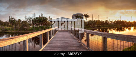 Sonnenuntergang über Pavillon auf einer hölzernen abgeschiedenen, ruhigen Promenade entlang einer Marsh Teich in Freedom Park in Naples, Florida Stockfoto