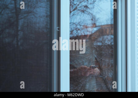 Allein Mann traurig über Handy SMS durch die Fenster im Winter am Nachmittag zu senden, während es schneit draussen, Blaugrün und Orange getönten Bild Stockfoto