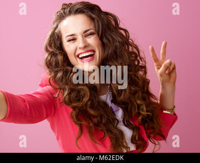 Rosa Stimmung. glückliche junge Frau mit langen Welligen brünette Haare auf Rosa unter selfie und Sieg isoliert Stockfoto