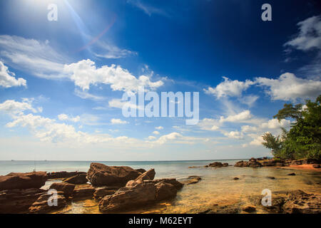 Flache transparent gelb steinigen Meeresgrund unter Ebbe gegen azurblauen Meer und blauen bewölkten Himmel Stockfoto