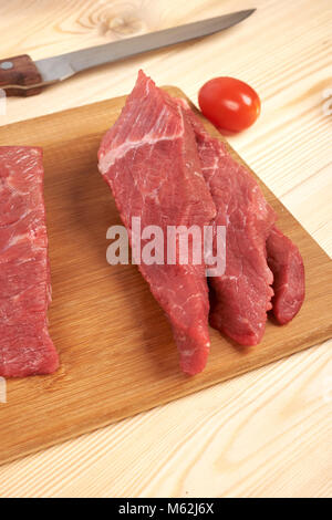 Geschnittenes rohes Rindfleisch auf Schneidebrett und Gemüse Stockfoto