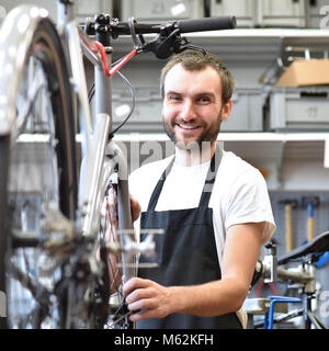 Porträt eines freundlichen und kompetenten Fahrradmechaniker in einer Werkstatt Reparaturen ein Fahrrad Stockfoto