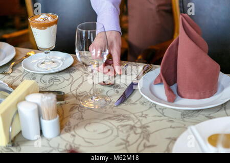 Kellner einen Tisch bereiten für das Frühstück. Hintergrund. Im Vordergrund von Servietten, Teller, Gläser. Ruhige Atmosphäre. Close Up. Hand passt die Löffel Stockfoto