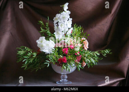 Asymmetrische Blumenstrauß aus Rosen, Nelken, Rittersporn und Hortensien auf braunem Hintergrund Stockfoto