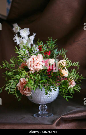 Asymmetrische Blumenstrauß aus Rosen, Nelken, Rittersporn und Hortensien auf braunem Hintergrund Stockfoto