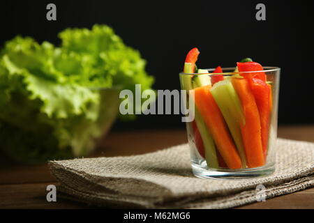 Paprika, Karotten, Sellerie, roh Gurken in Streifen schneiden. In ein Becherglas. Daneben sind Salatblätter, Basilikum. Auf dem Hintergrund der Tuch, Sackleinen, Stockfoto