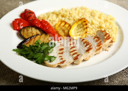 Gegrilltes Hähnchen mit Scheiben, mit Gemüse, Bulgur auf einer weißen Platte, mit Petersilie dekoriert. Kalorienarme, diätetische Lebensmittel für einen gesunden Lebensstil. Clos Stockfoto