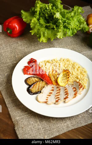 Gegrilltes Hähnchen mit Scheiben, mit Gemüse, Bulgur auf einem weißen Teller. Im Hintergrund, Salatblätter, Farbe Pfeffer. Kalorienarme, diätetische Lebensmittel für Stockfoto