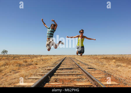 Junge backpacker Paar auf die Bahn in der Wüste im Outback Australien springen. Spaß, Reisen, Abenteuer Konzept erkunden Stockfoto