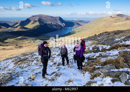 Vier Freunde Wandern auf Rhyd Ddu Pfad auf den unteren Hängen des Snowdon mit Schnee im Winter in Snowdonia National Park und der Küste. Gwynedd, Wales, Großbritannien Stockfoto