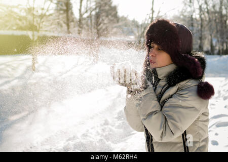 Hält eine Frau eine Handvoll Schnee in den Händen und bläst. Winter im Wald. Die sonne funkelt. Tag, Russland. Stockfoto