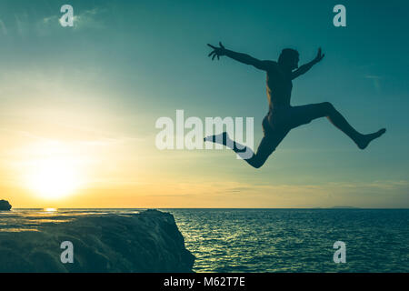 Mann über eine Klippe ins Meer springen auf Sonnenuntergang in Koh Phangan Island, Thailand. Vintage Effekt. Drei von drei Serien Stockfoto