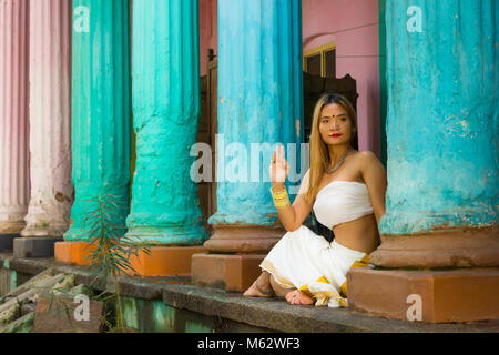 Indische yogi Mädchen mit traditionellen Kerala Sari in Ardha Matsyendrasana darstellen. Junge Frau übt Yoga auf die Hälfte der Wirbelsäule verdreht, von bunten Spalten Stockfoto