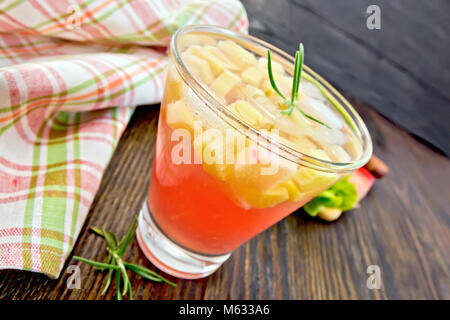 Limonade mit Rhabarber und Rosmarin in einem Glas, Stiele und ein Blatt eines pflanzlichen, kariert Serviette auf einem Holzbrett Hintergrund Stockfoto