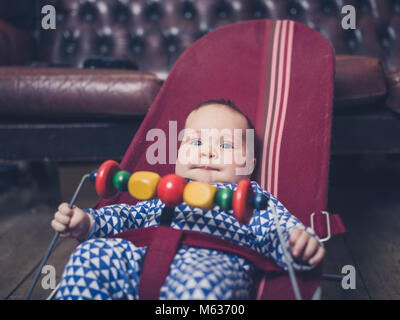 Ein Baby sitzt in einem Vintage bouncy Stuhl auf dem Holzboden Stockfoto