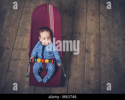 Ein Baby sitzt in einem Vintage bouncy Stuhl auf dem Holzboden Stockfoto